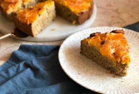 A mixed citrus olive oil cake with a plate in the forefront with a slice cut from the cake