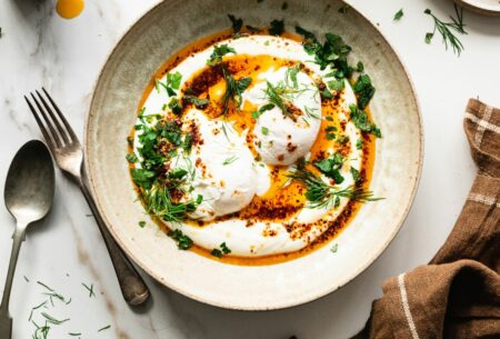 A bowl of prebiotic Turkish eggs topped with sprigs of dill and mint and a drizzle of chilli oil.