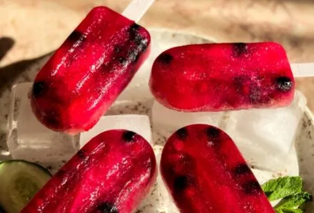 Four red fermented fizz ice lollies lying on ice cubes on a tray in the sunlight