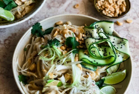 Satay noodles with ribbons of courgette, roasted peanuts, lime and sauerkraut and black sesame seeds with a bowl of peanuts in the background