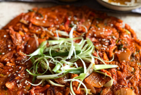 Kimchi pancake with spring onion shavings and soy sauce dip in the background