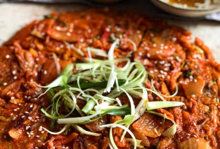 Kimchi pancake with spring onion shavings and soy sauce dip in the background