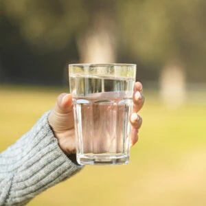 Photo of someone with a grey jumper sleeve holding a glass of water outdoors to reflect the diet myth of drinking with food