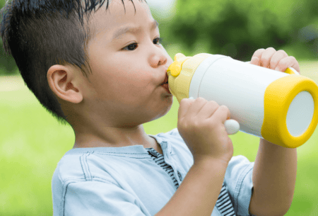 Image shows child standing outside holding a drink bottle to mouth.
