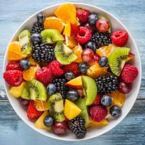 Photo of a bowl of fruit on a wooden table from a top angle, including blackberries, kiwi slices, blueberries, orange segments and raspberries to reflect diet myth of avoiding fruit