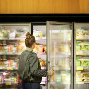 Photo of a woman with her hair up opening a freezer door in a shop with frozen vegetables in the background to reflect diet myth of fresh food is better for you
