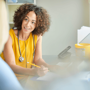 Photo of a GP — a smiling woman in a yellow top looking at a patient offscreen to reflect bloating management