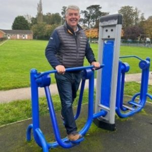 An image of Selwyn smiling. He's using a piece of gym equipment in the park.