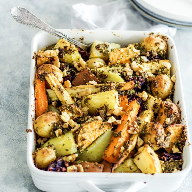 Large oven baking dish full with roasted potatoes and parsnips, mixed with walnut pesto