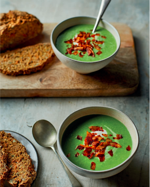 Two bowls of super green pea and ‘ham’ soup, with fresh bread on a chopping board