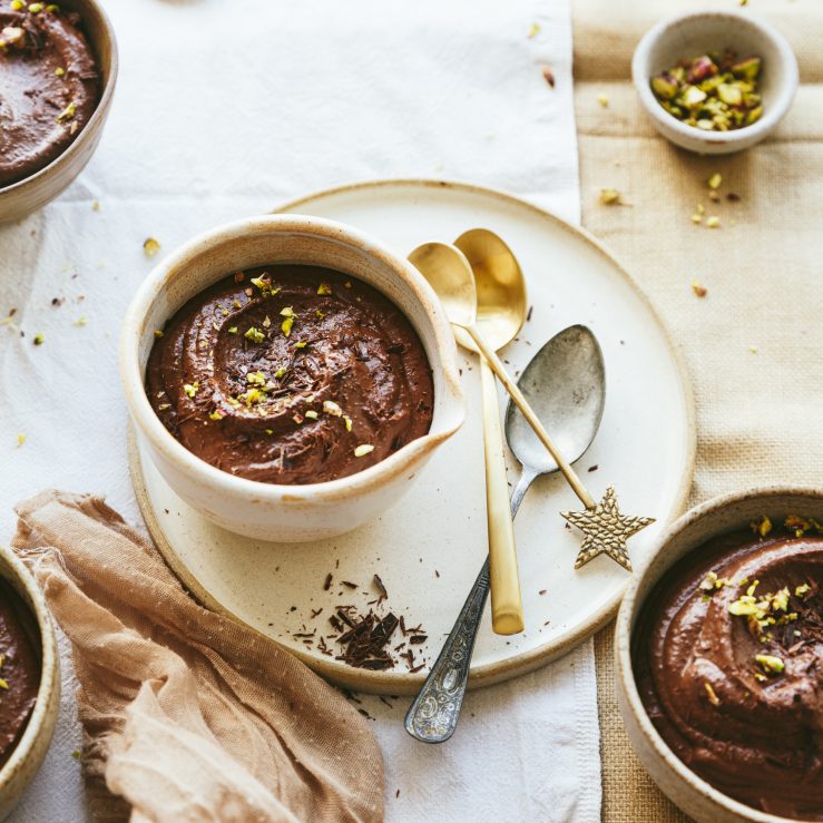 A small pot of pistachio and chocolate mouse on a plate with 3 spoons