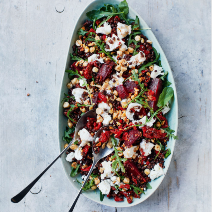 A oval shaped bowl with beetroot, lentil, goats cheese, rocket and hazelnuts