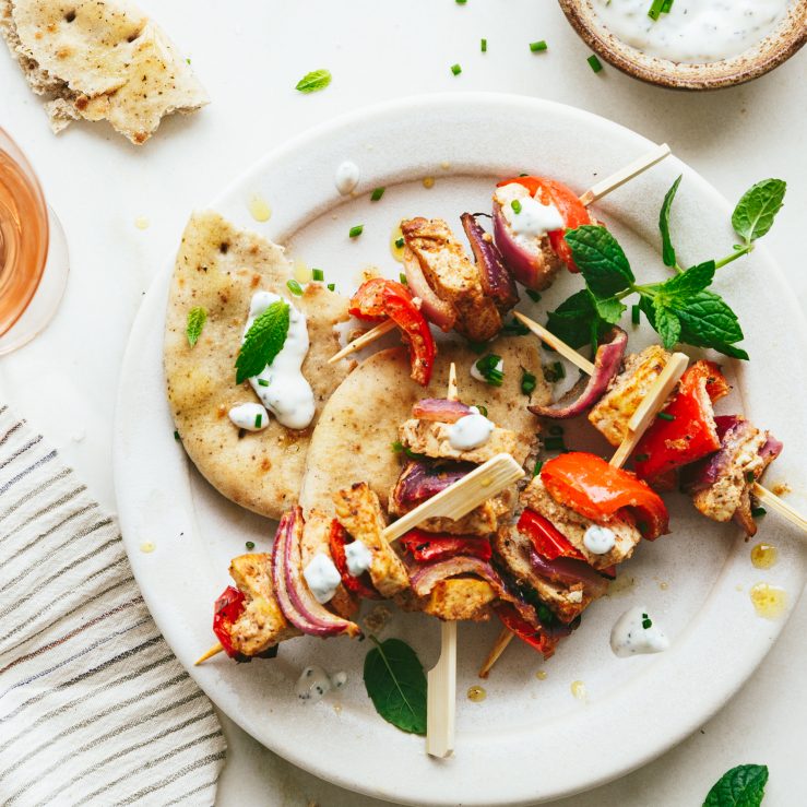 A white plate with torn pitta bread and spiced tofu and pepper skewers with mint yogurt and sprigs of mint