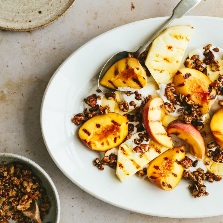 A white plate with yogurt, grilled peached and walnuts