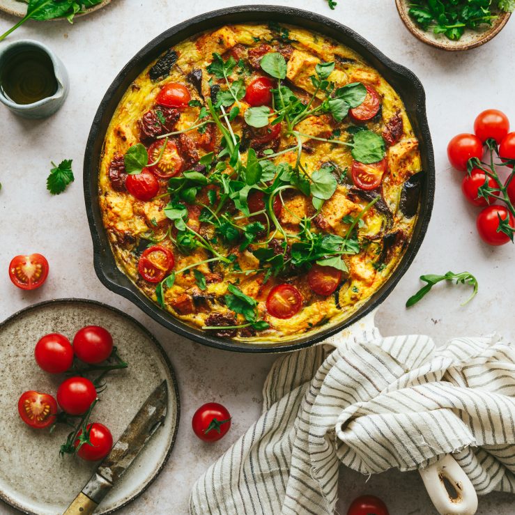 A pan filled with Mediterranean tofu frittata with tomatoes and rocket and dressing all around the pan