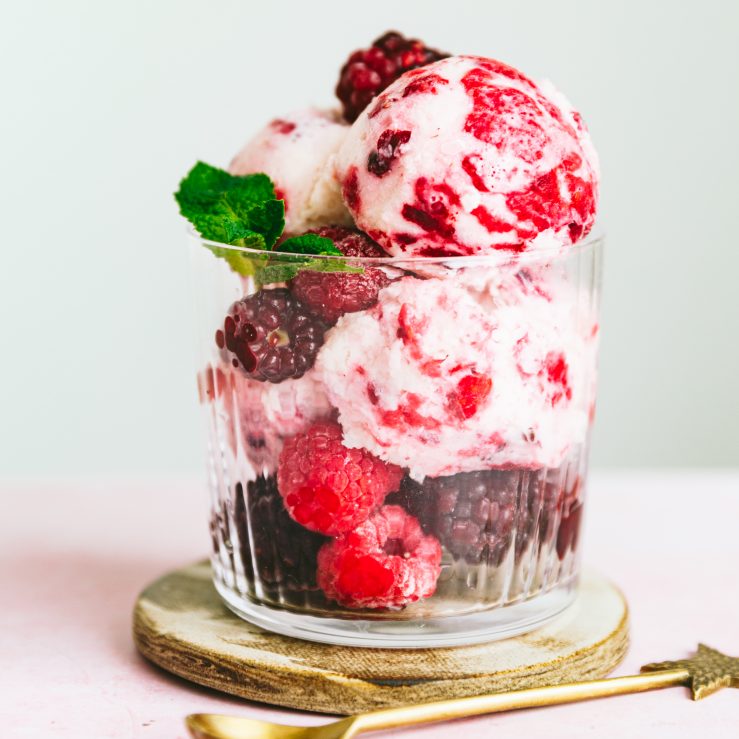 A glass filled with mixed berry kefir ice cream with fresh raspberries and blueberries and a sprig of mint