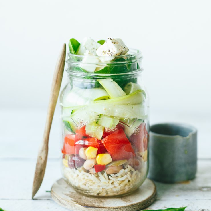 A glass jar containing rice, sweetcorn, mixed beans, peppers, cougette ribbons, spinach and feta