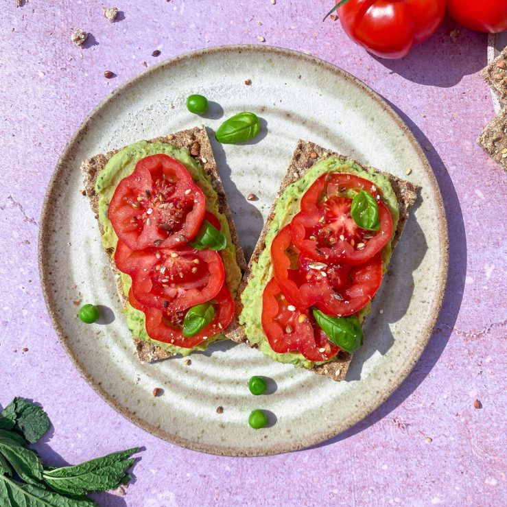 Two crackers with a pea and mint hummus and fresh tomatoes and basil on a grey plate