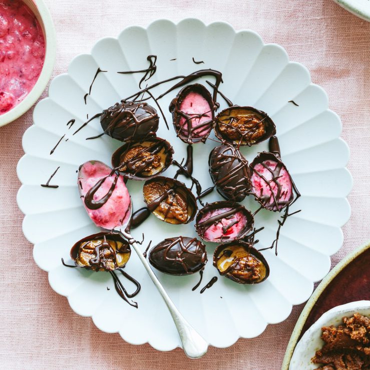 A plate of small dark chocolate easter eggs filled with raspberry and live yogurt or nut butter with a drizzle of chocolate on top