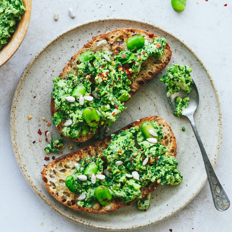 A plate with two slices of toast spread with broad bean dip chilli and sunflower seeds