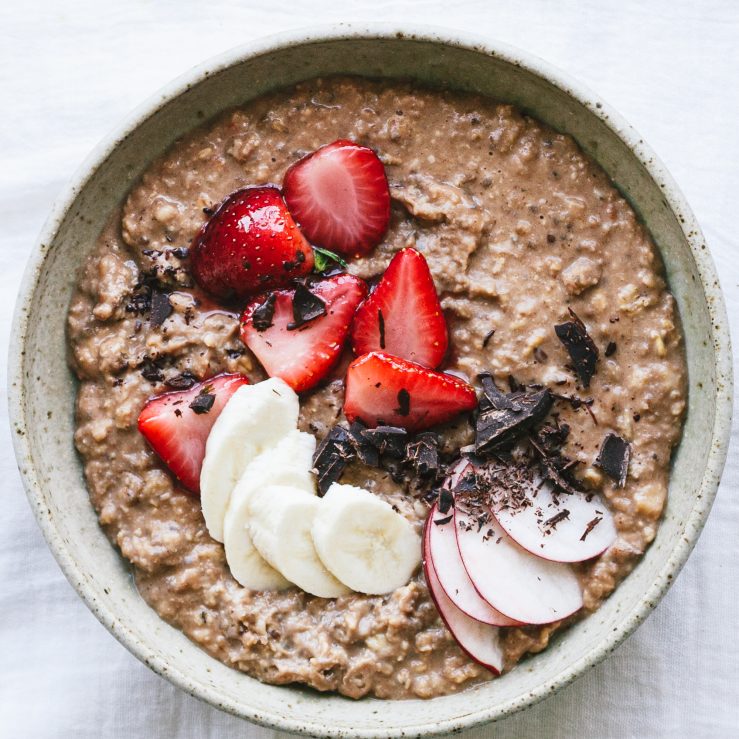 A bowl of creamy chocolate porridge topped with strawberries, sliced banana and grated chocolate