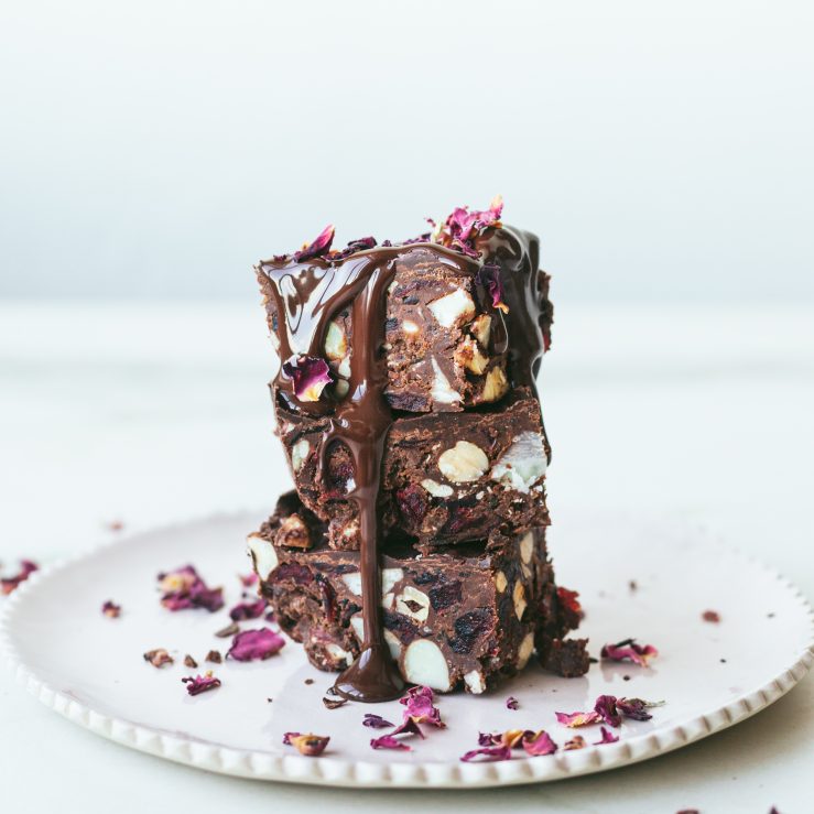 A stack of 3 fruit and nut love bites with a drizzle of chocolate and rose petals on a white plate