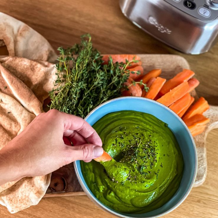 Wooden board with carrot battons, thyme and flatbreads and a bowl of pistachio and white bean dip