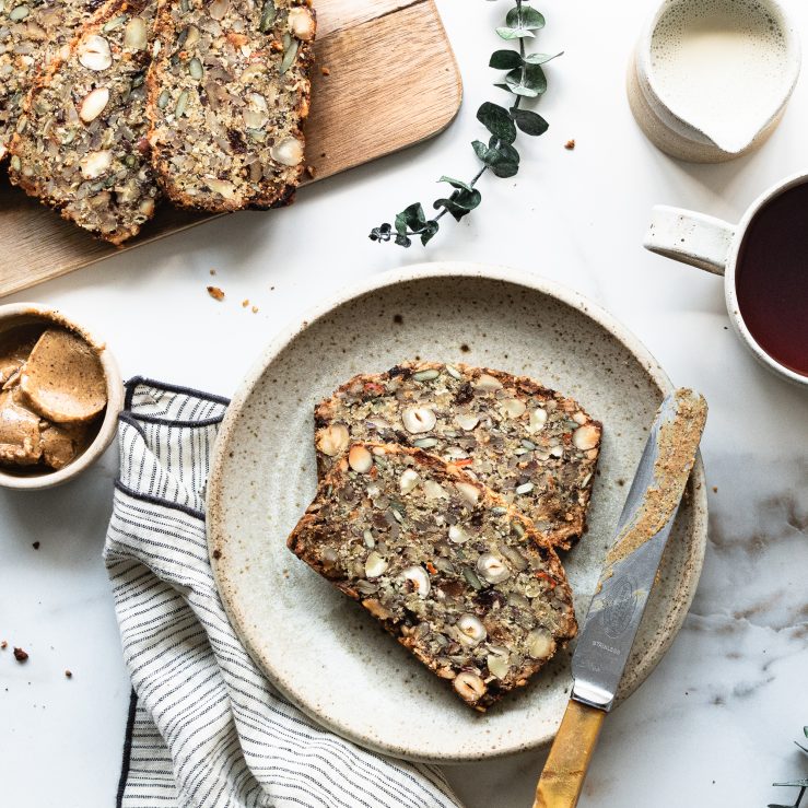 Two pieces of Nordic style super seedy and nutty loaf with figs, with knife and nut butter spread