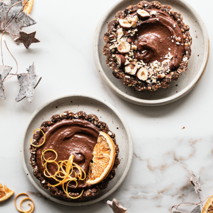 Two chocolate granola tarts on plates, decorated with fresh fruit and nuts