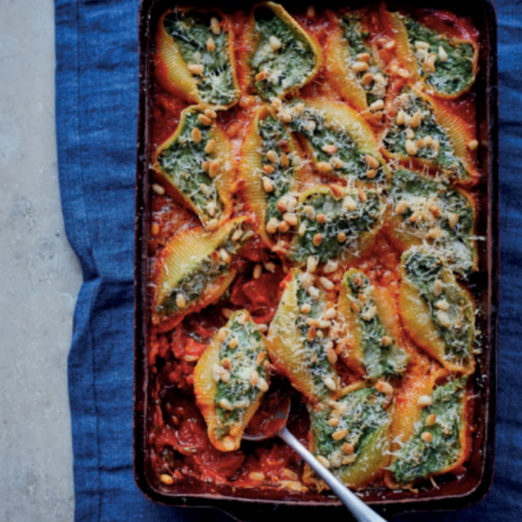 Spinach and ricotta stuffed pasta shells with toasted pine nuts on top in a oven proof dish with a spoon in the dish to serve