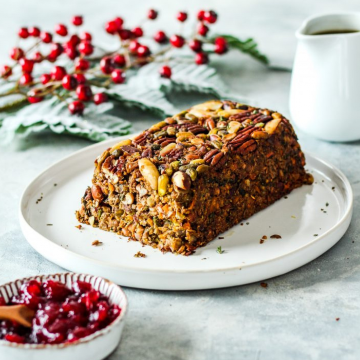 A large plate showing a festive nut roast with a side jug of gravy and small bowl of cranberry sauce