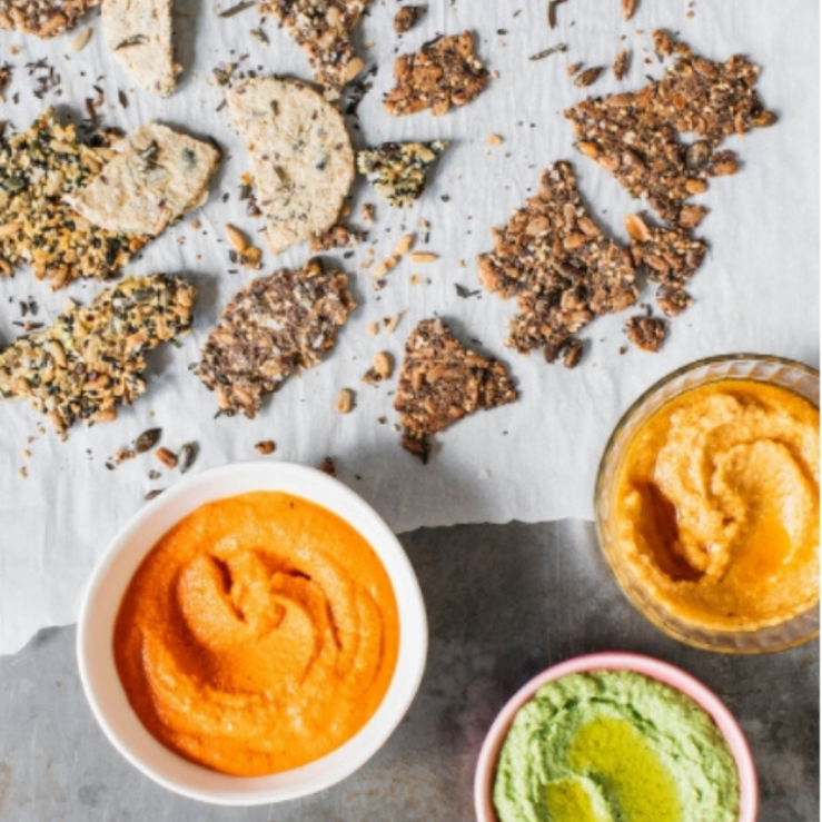Broken up seeded crackers with small bowls of harissa red pepper dip