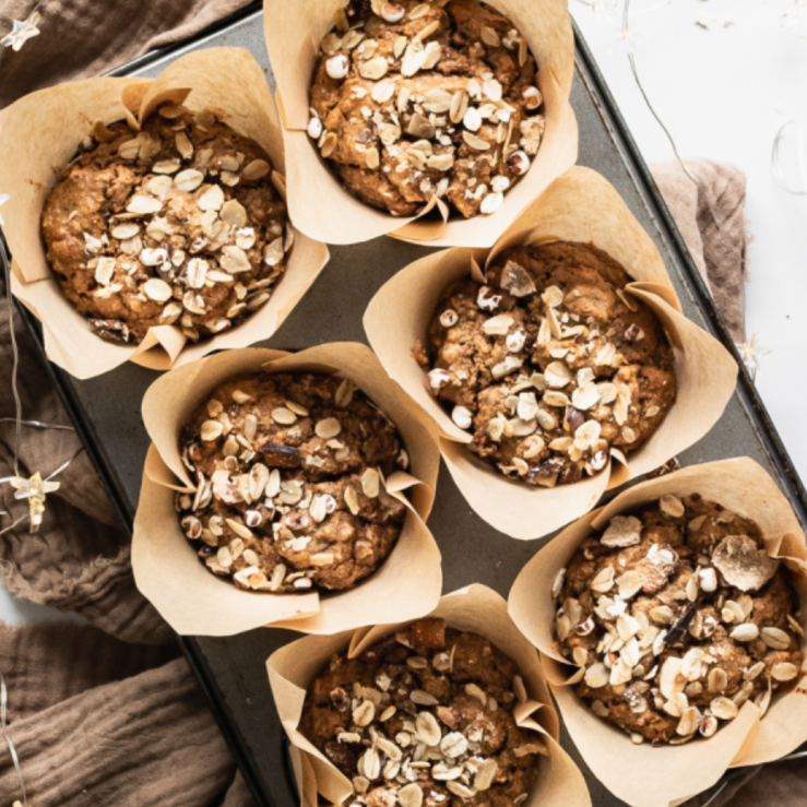 Six freshly baked gingerbread muffins in a muffin tray, sprinkled with granola