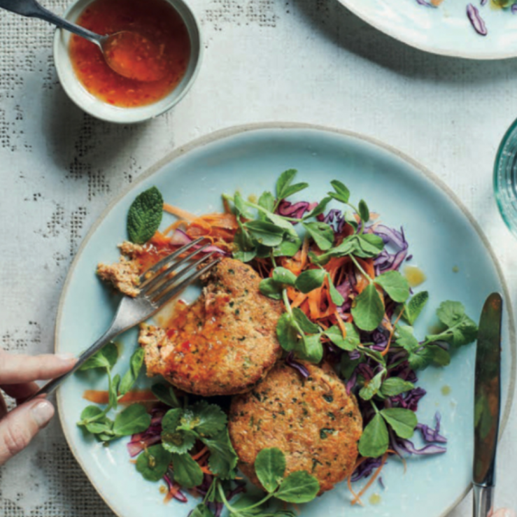 Two cooked fishcakes on top of a fresh, crunchy salad with a pot of homemade dressing