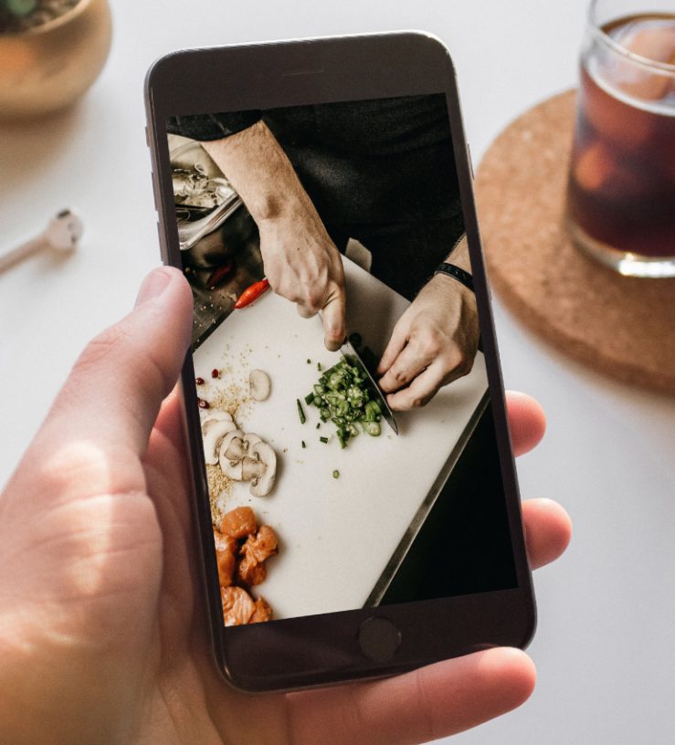 Someone holding a mobile phone with an image of food preparation on the screen