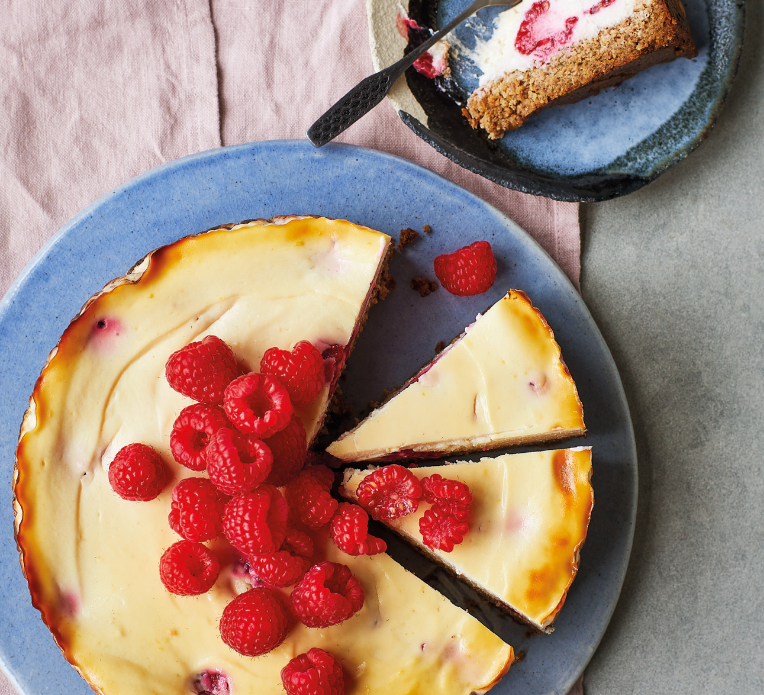 A raspberry cheesecake with fresh raspberries on top with two slices cut