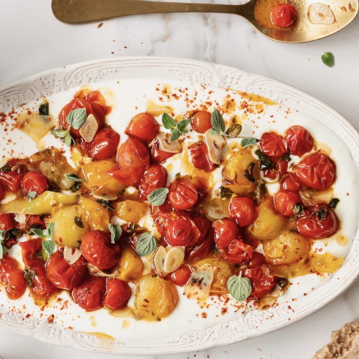 Red and orange cooked tomatoes displayed over cold yogurt on a long, ceramic plate