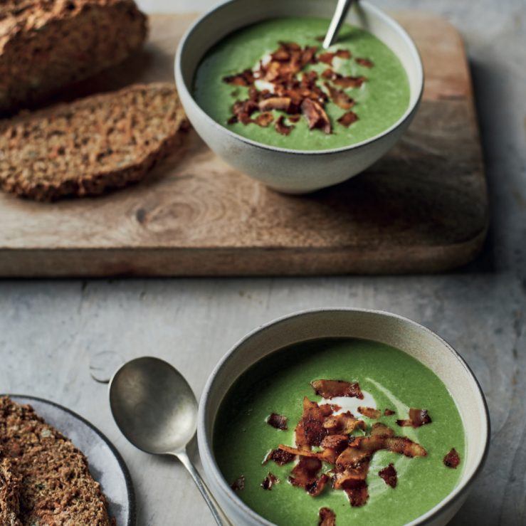 Fresh baked brown wheaten bread displayed on a chopping board with a bowl of soup