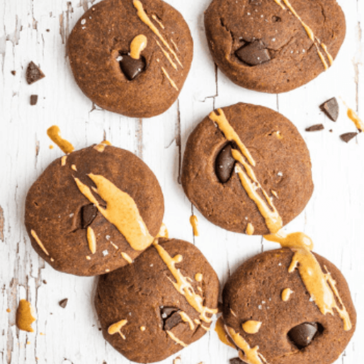 Six chocolate & peanut butter teff cookies on bench top with chocolate chunks and peanut butter drizzle