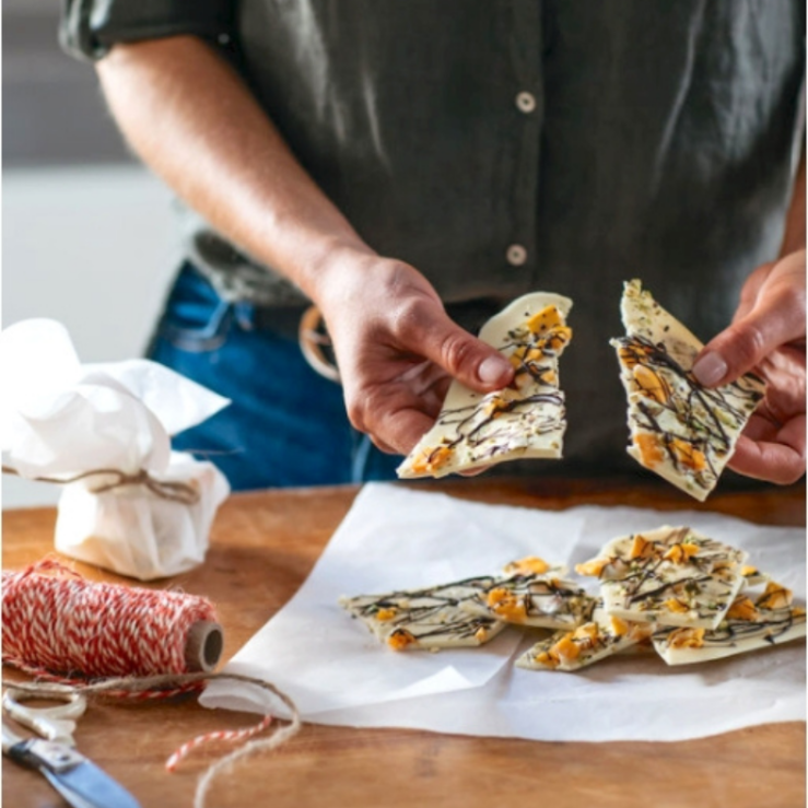 One large piece of prebiotic chocolate bark being broken in half, topped with mango, pistachios and dark chocolate