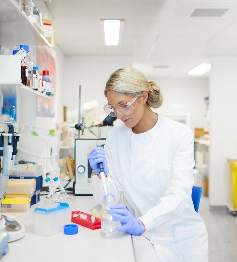 Photo of Dr Megan Rossi, founder of The Gut Health Doctor, sitting in a lab looking and using a test tube