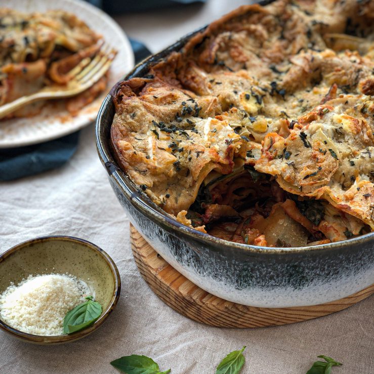 Large serving dish on bench filled with fresh cooked lasagne, one piece cut away to show inside