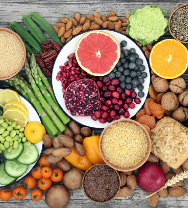 Photo of a table with lots of different plant groups spread out on top, i.e. fruits, wholegrain rice, bread, vegetables, legumes, etc.