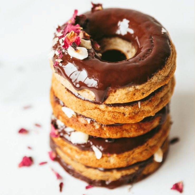A stack of chocolate breakfast donuts sprinkled with rose petals and hazelnuts