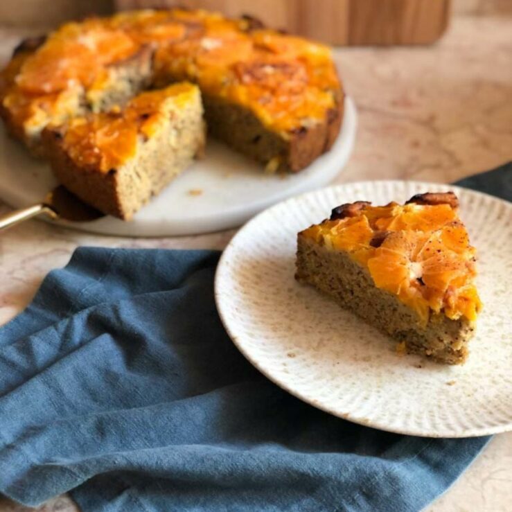 A mixed citrus olive oil cake with a plate in the forefront with a slice cut from the cake