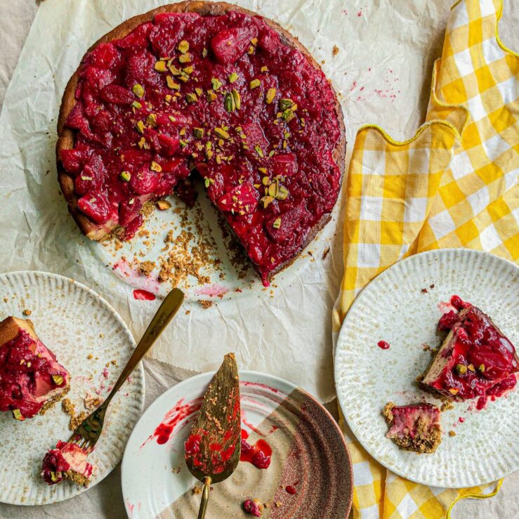 Photo of strawberry and pistachio cheesecake and two plates with slices of cheesecake that are half eaten