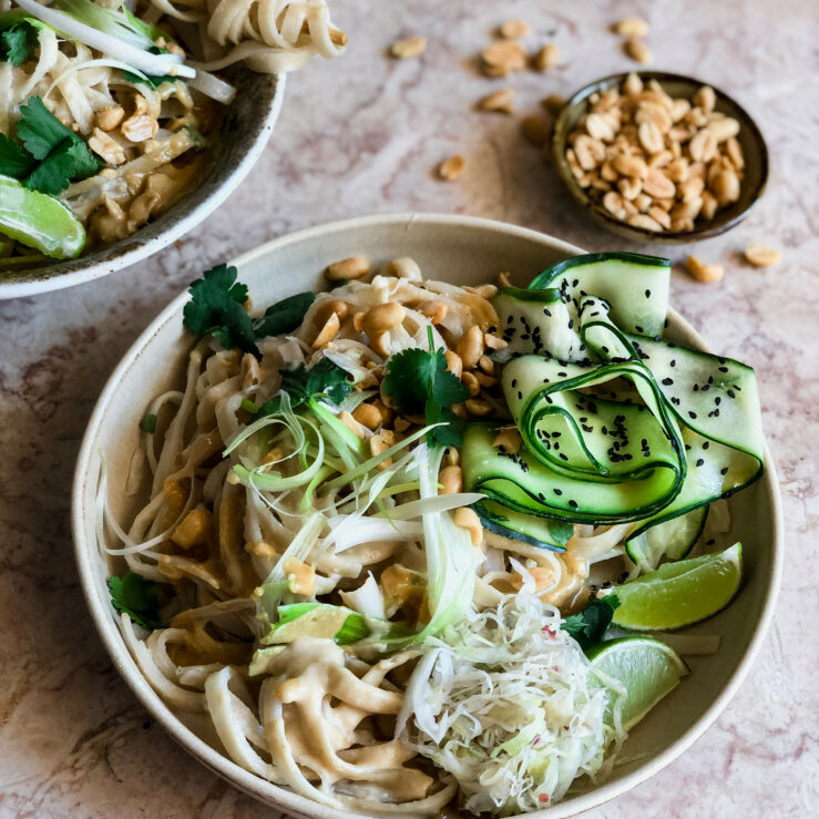 Satay noodles with ribbons of courgette, roasted peanuts, lime and sauerkraut and black sesame seeds with a bowl of peanuts in the background