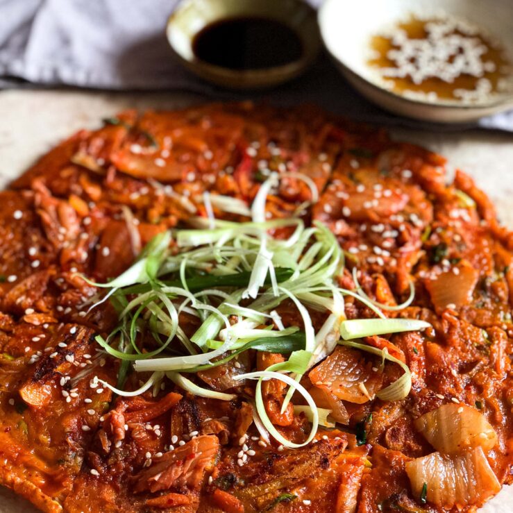 Kimchi pancake with spring onion shavings and soy sauce dip in the background