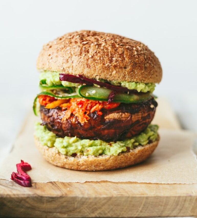 Photo of a spicy miso mushroom burger with lots of salad sitting on a wooden block