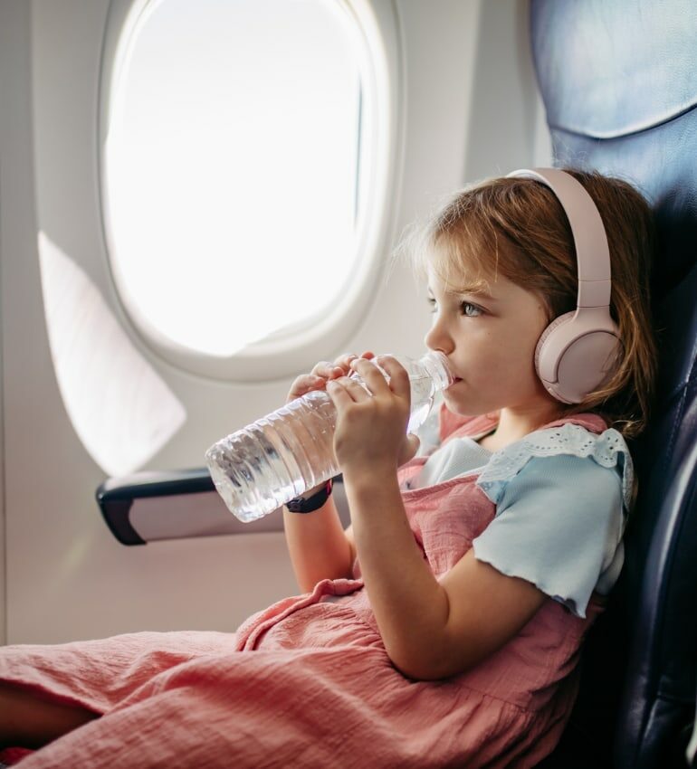 Photo of a young girl drinking a bottle of water on an airplane to show hydration to support gut health on holiday